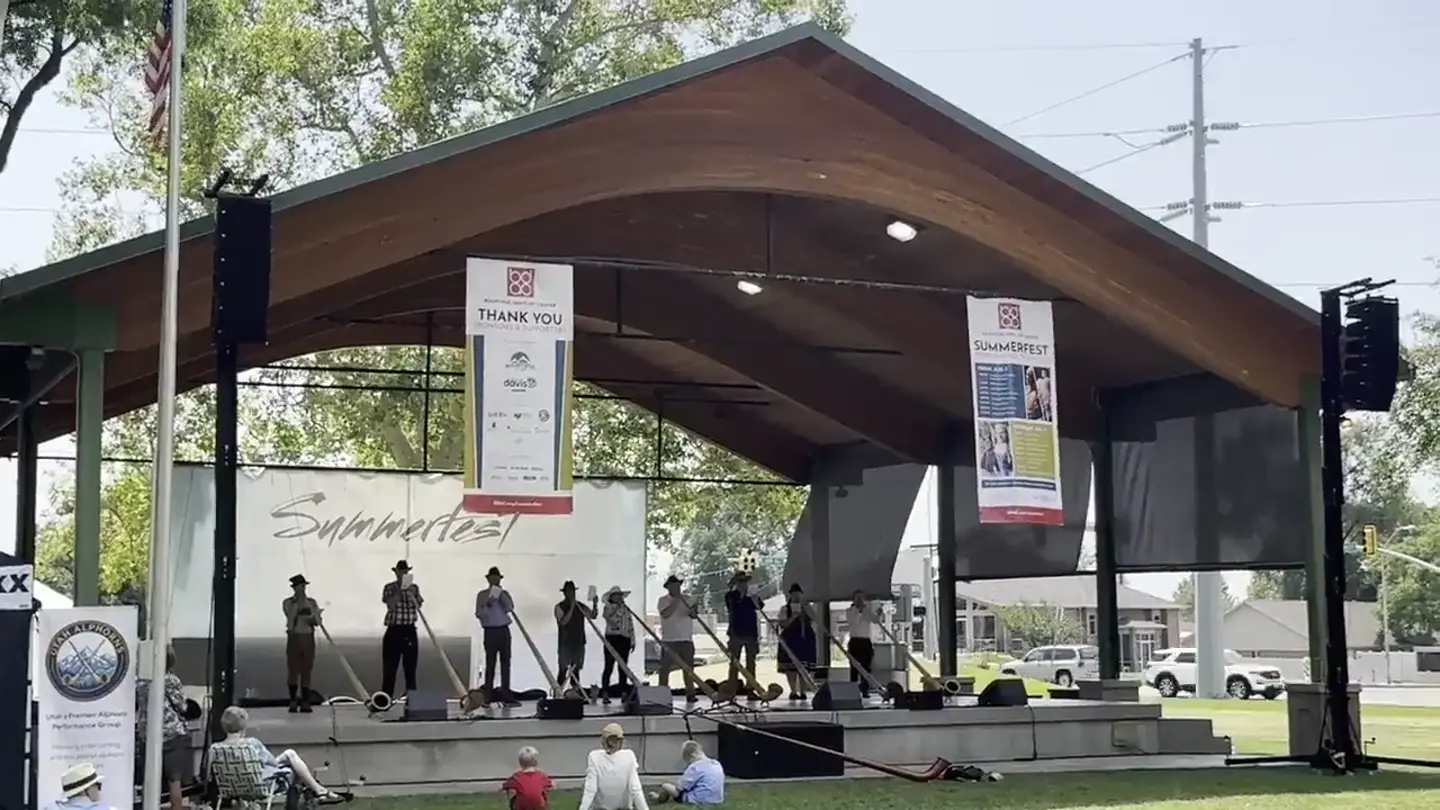 Polynesian dance group performing with ipu gourds on an outdoor festival stage with SwissMixx Audio stage monitors across the front
