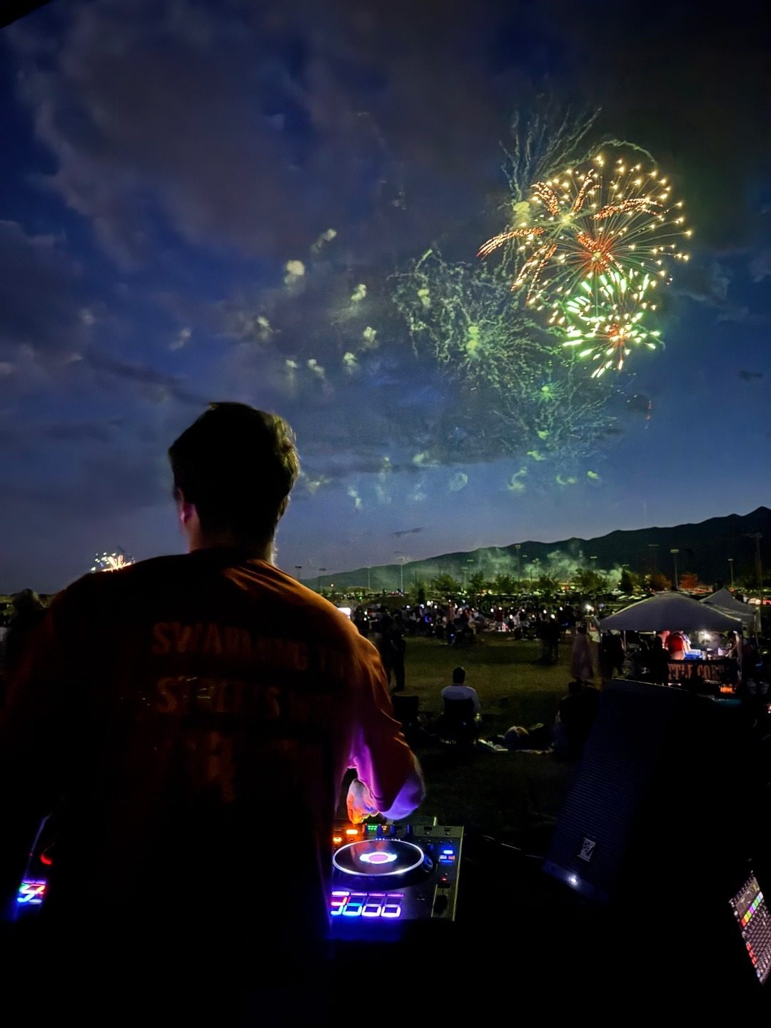 Fireworks exploding over a large crowd at night with DJ in foreground