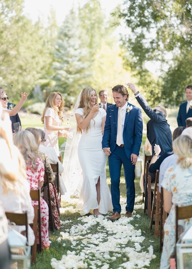 Bride and groom walking back up a petal covered aisle as guests celebrate