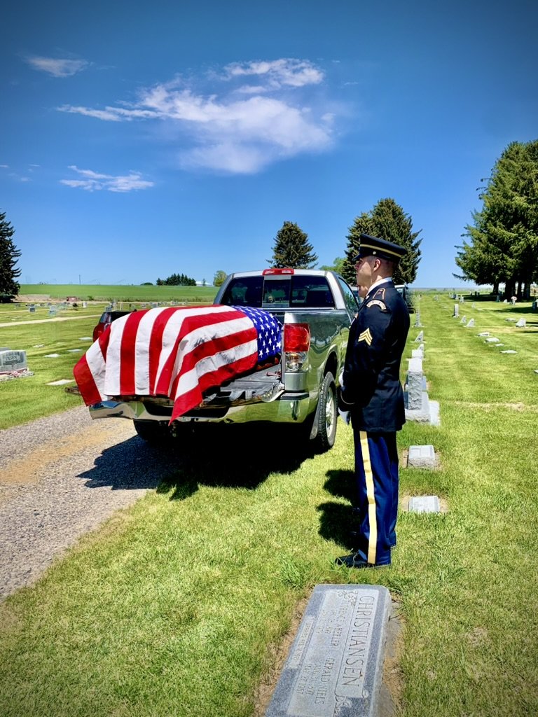 A military honor guard salutes a flag-draped casket at a graveside service