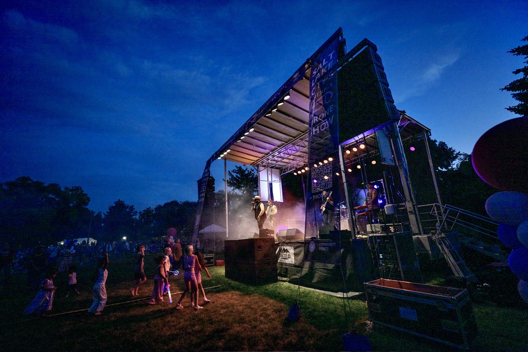 Nighttime community concert crowd with kids holding glow sticks in front of the SwissMixx stage in Salt Lake