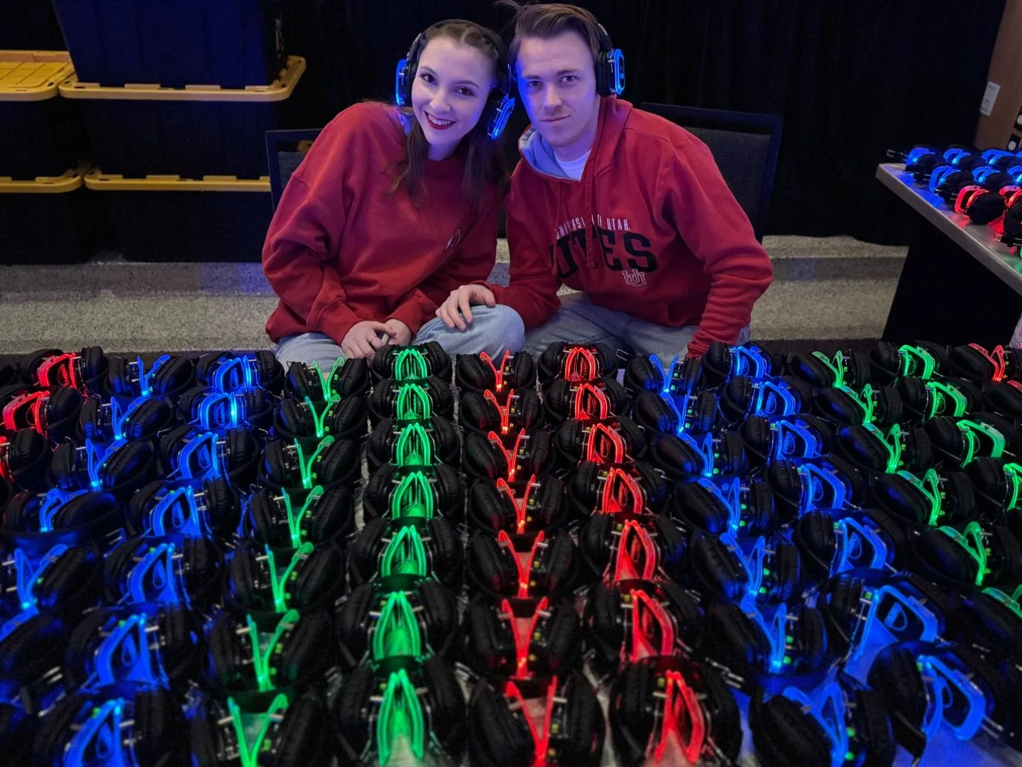 Couple wearing SwissMixx Audio 3-channel LED silent disco headsets at event in Utah with full fleet of 3-color headsets on display, rental in Treasure Valley Idaho up to 300 guests