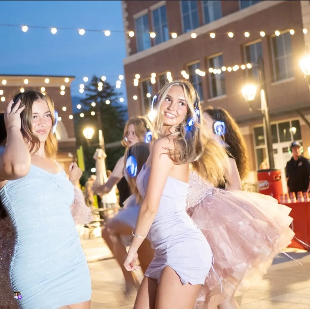 Guests dancing at an outdoor silent disco in Logan City Utah wearing glowing LED wireless headsets under string lights
