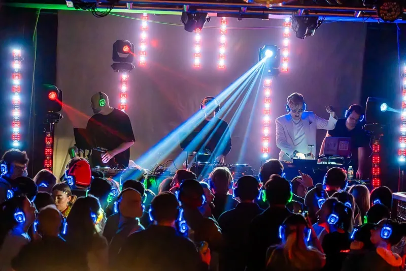DJ with light beams over a silent disco crowd in glowing headphones, SwissMixx Audio silent disco