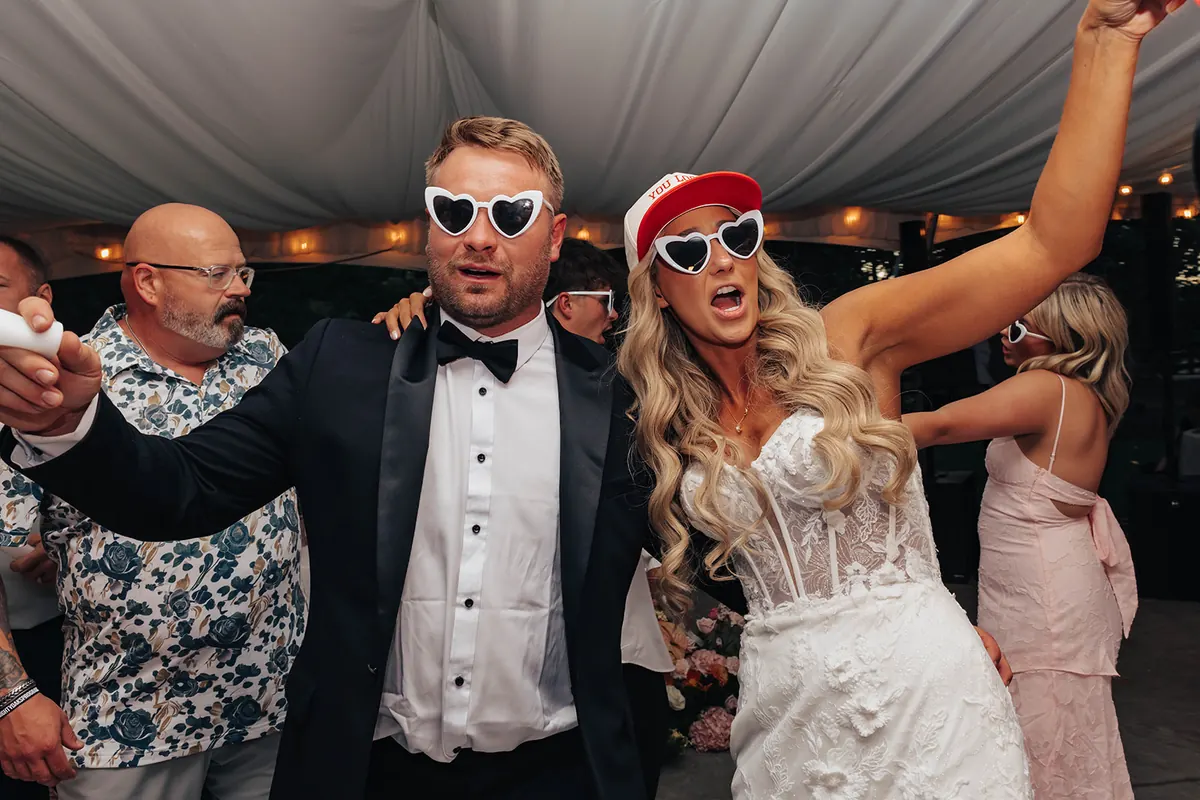 Bride and groom in heart sunglasses dancing with their guests on a checkerboard dance floor